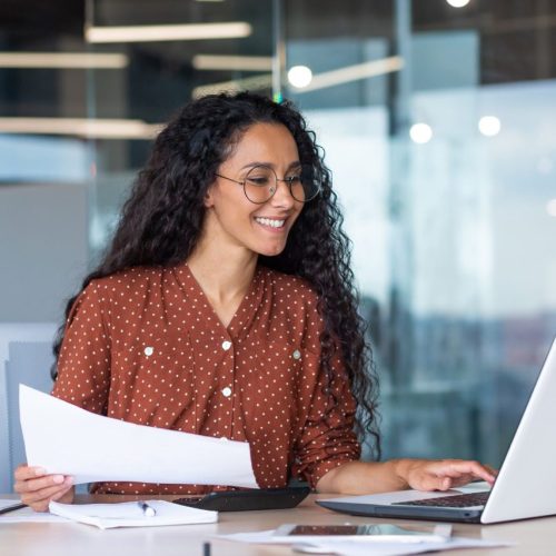 latin american businesswoman working inside office with documents and laptop, worker paperwork calculates financial indicators smiling and happy with success and results of achievement and work